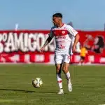 Joven futbolista sosteniendo documentación de contrato en un moderno estadio de fútbol.