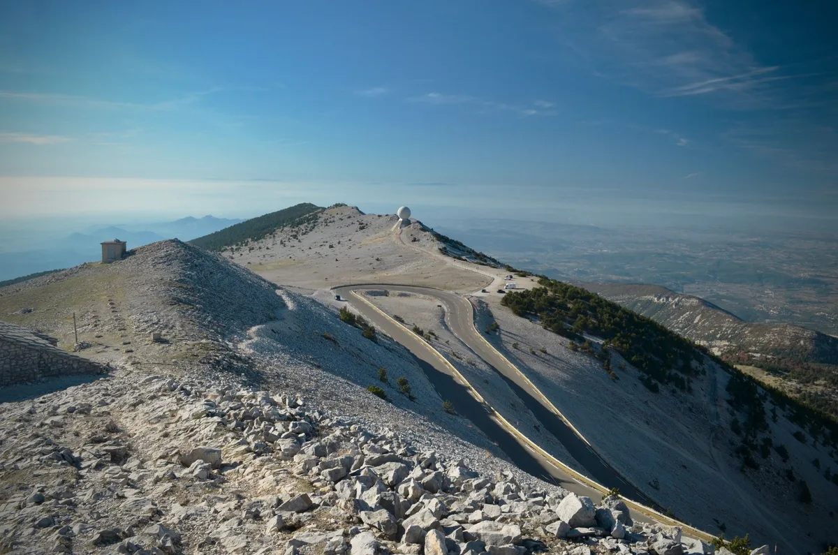 Ciclista cruzando la meta en una subida de montaña con paisaje alpino de fondo