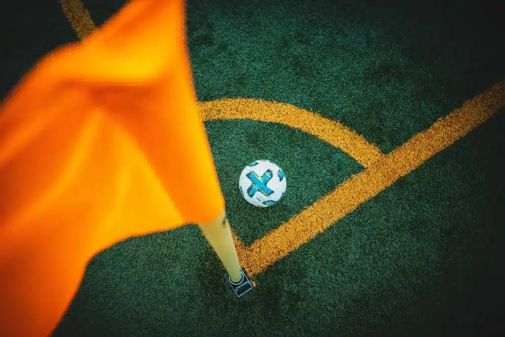 Pelota de fútbol en primer plano con graderío y siluetas de manos aplaudiendo en un estadio iluminado